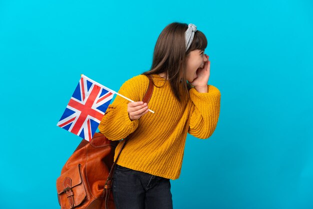 Kleines Mädchen, das Englisch studiert, isoliert auf blauem Hintergrund, der mit dem Mund weit offen zur Seite schreit