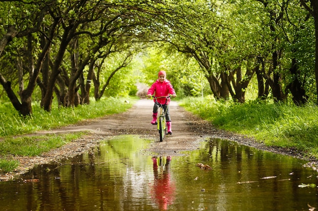 kleines Mädchen, das Fahrrad in der Wasserpfütze fährt