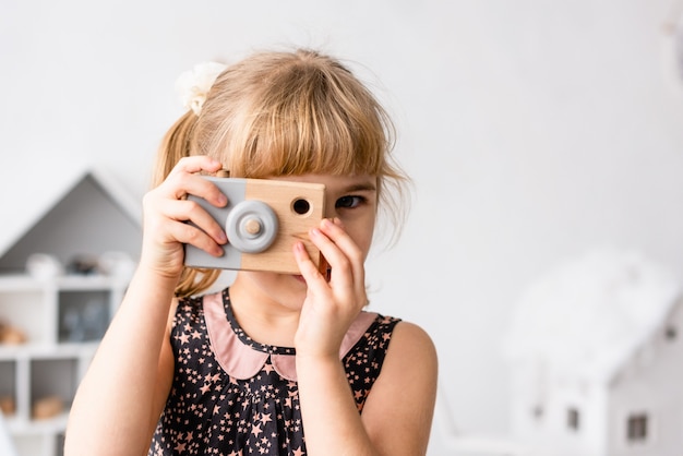 Kleines Mädchen, das Foto mit Spielzeugphotokamera drinnen macht