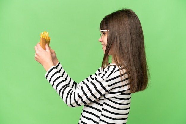 Kleines Mädchen, das gebratene Chips über isoliertem Chroma-Key-Hintergrund mit glücklichem Ausdruck hält