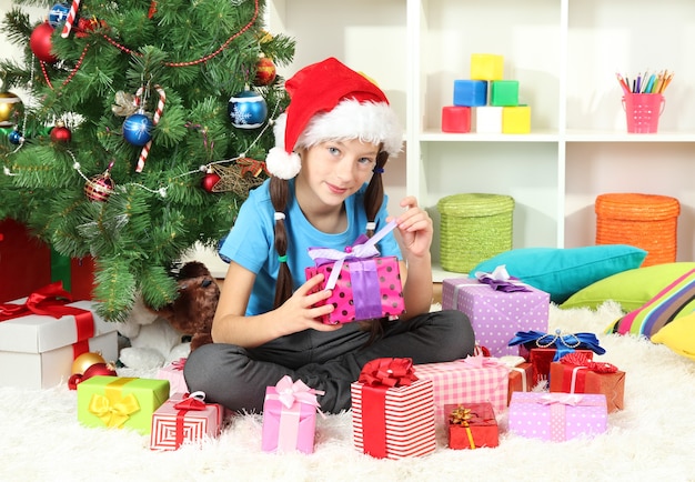 Kleines Mädchen, das Geschenkbox nahe Weihnachtsbaum hält