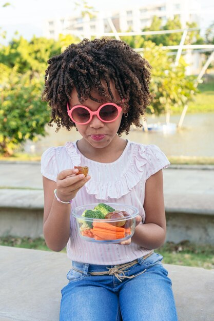 Kleines Mädchen, das gesundes Essen in einem Park isst Familienlebensstilkonzept