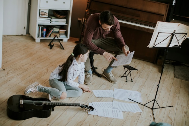 Kleines mädchen, das gitarre mit ihrem musiklehrer in der rustikalen wohnung spielt