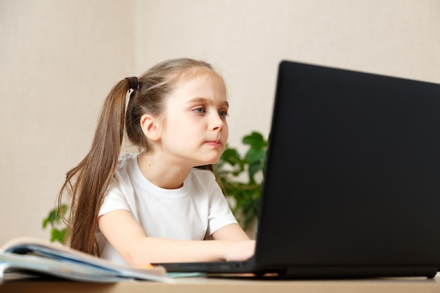 Kleines Mädchen, das ihre Hausaufgaben zu Hause macht und einen Laptop benutzt