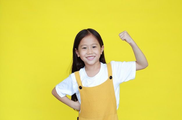 Kleines Mädchen, das ihre Muskeln auf gelbem Hintergrund zeigt