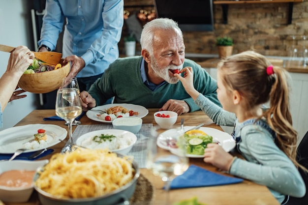 Kleines Mädchen, das ihren Großvater füttert, während es mit der Familie im Speisesaal zu Mittag isst Der Fokus liegt auf dem älteren Mann