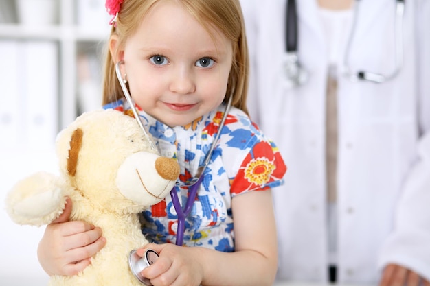 Foto kleines mädchen, das ihren teddybären mit stethoskop untersucht vertrauenskonzept für kinderpatienten im gesundheitswesen