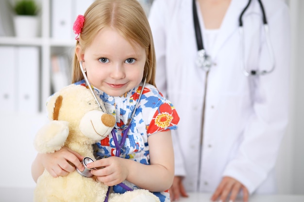 Kleines Mädchen, das ihren Teddybären mit Stethoskop untersucht Vertrauenskonzept für Kinderpatienten im Gesundheitswesen