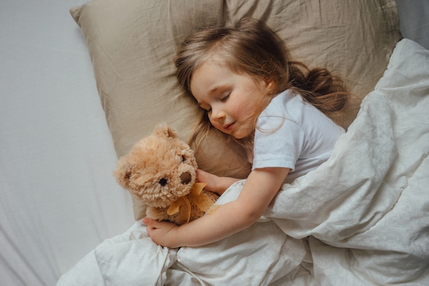 Foto kleines mädchen, das im bett schläft, umarmt kuscheltier zu hause, ansicht von oben