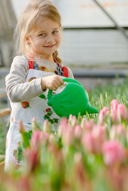 Kleines Mädchen, das im Frühjahr Blumen in einem Gewächshaus gießt.