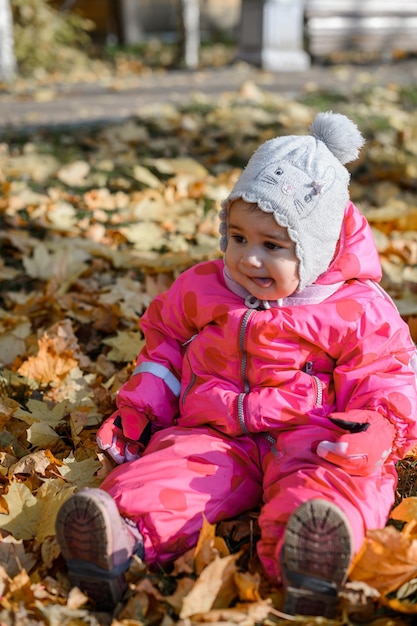 Kleines Mädchen, das im Herbst auf gelben Blättern auf dem Boden sitzt