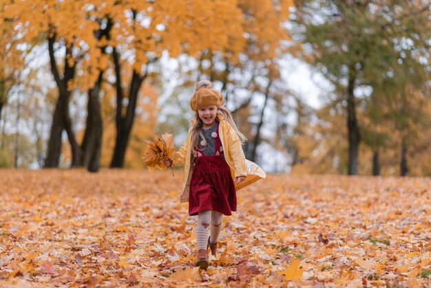 Foto kleines mädchen, das im park mit blatt-herbst-naturgarten geht