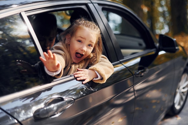 Kleines Mädchen, das im schwarzen Auto sitzt und durch das Fenster schaut