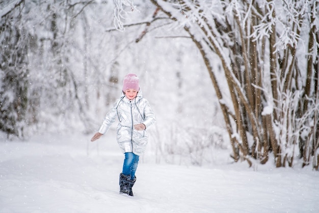 Kleines Mädchen, das im Winter im verschneiten Park läuft