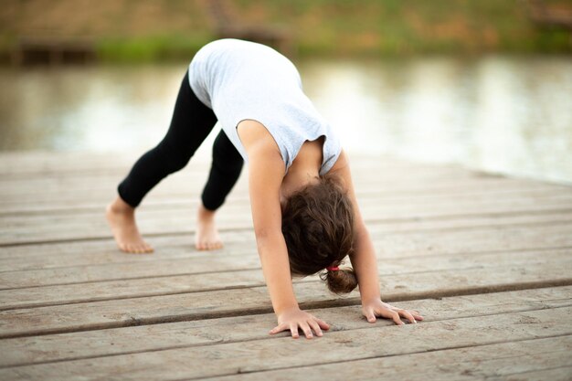 Kleines Mädchen, das in der Natur in der Nähe von Fluss oder See sitzt und Yoga praktiziert Gesunder Lebensstil