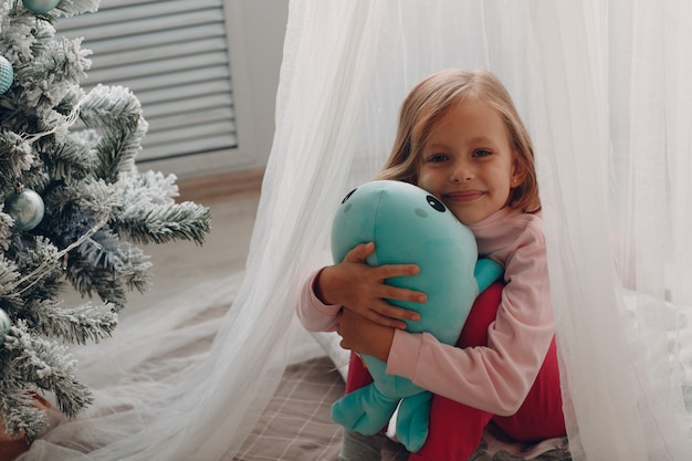 Kleines Mädchen, das in einem Kinderzimmer mit einem Spielzeug sitzt