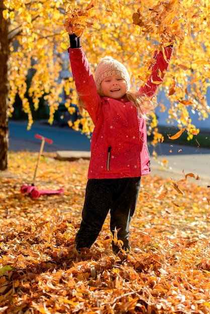 kleines Mädchen, das mit Blättern im Herbstpark spielt
