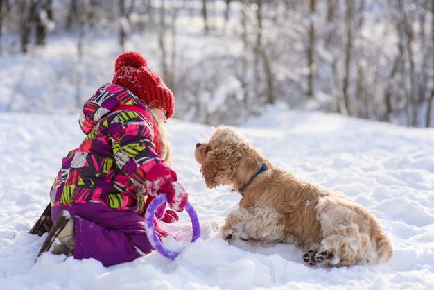 Kleines Mädchen, das mit Cockerspaniel im Schnee draußen spielt