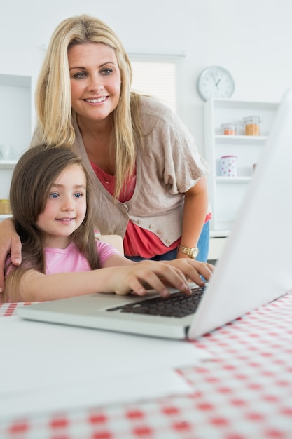 Kleines Mädchen, das mit der Mutter aufpasst am Laptop schreibt