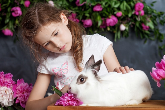 Kleines Mädchen, das mit echtem Kaninchen spielt. Kind und weißer Hase an Ostern. Kinder und Haustiere spielen. Spaß und Freundschaft für Tiere und Kinder.