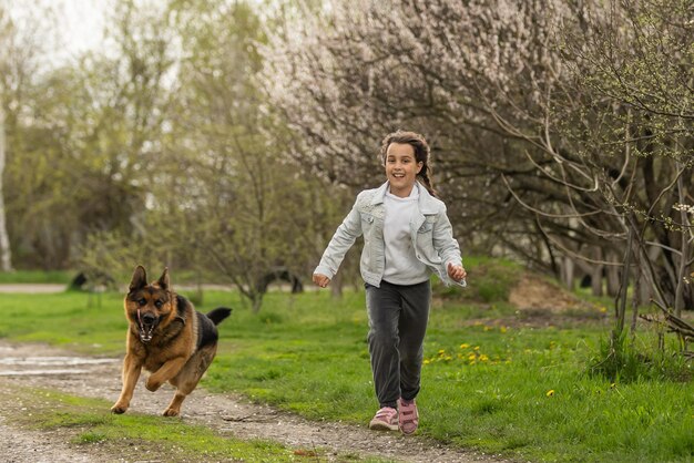 Kleines Mädchen, das mit einem Hund in einem Blumengarten läuft