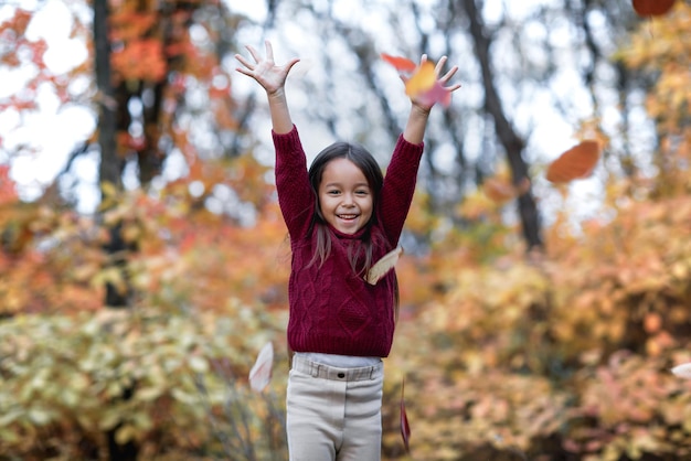 Kleines Mädchen, das mit gefallenen Blättern des Herbstes spielt