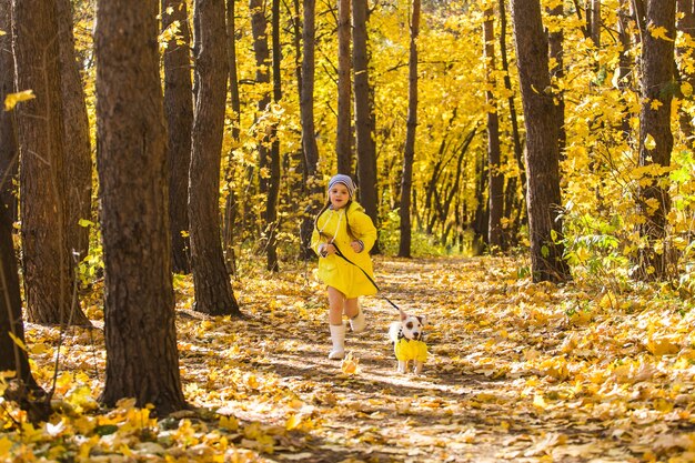 Kleines Mädchen, das mit ihrem Hund im Herbstwald spielt