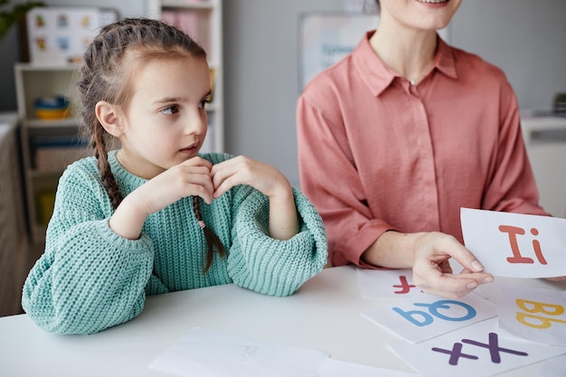 Kleines Mädchen, das mit Lehrer am Tisch sitzt und während einer Lektion Englisch lernt