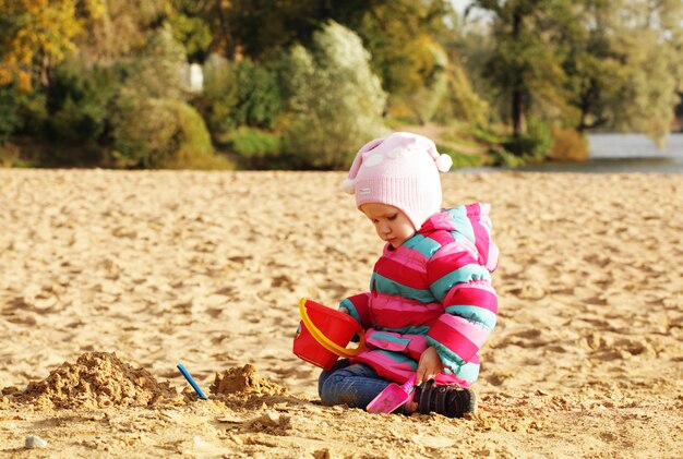 Kleines Mädchen, das mit Sand am Herbststrand spielt