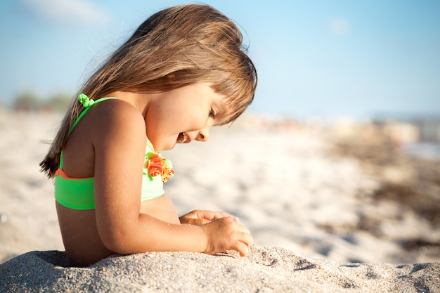 Kleines Mädchen, das mit Sand am Strand sitzt und spielt