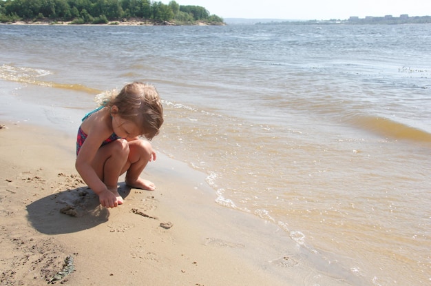 Kleines Mädchen, das mit Sand am Strand spielt