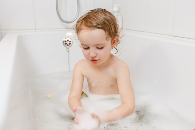 Kleines Mädchen, das mit Schaum in einer Badewanne badet.