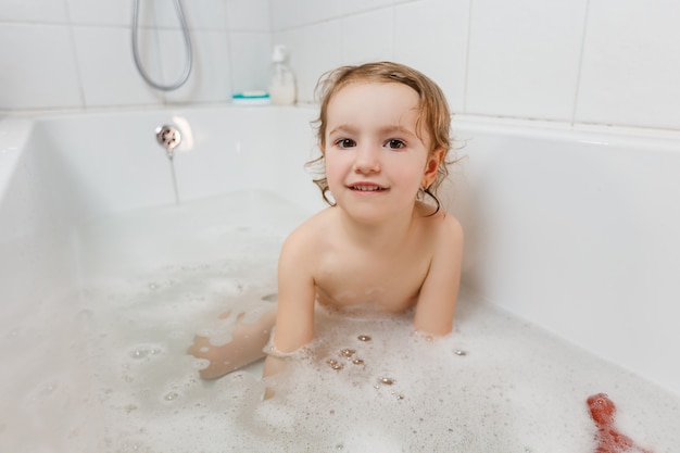 Kleines Mädchen, das mit Schaum in einer Badewanne badet.