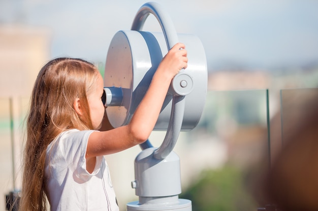 Kleines Mädchen, das münzbetriebenes Fernglas auf Terrasse mit schöner Ansicht betrachtet