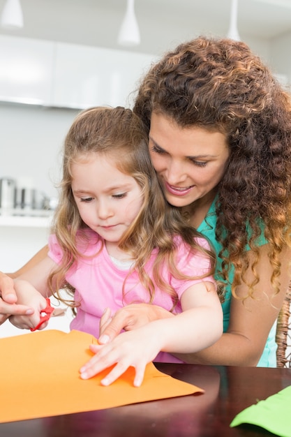 Kleines Mädchen, das Papierformen mit Mutter am Tisch macht