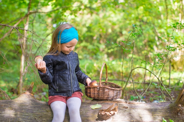 Kleines Mädchen, das Pilze in einem Herbstwald erfasst