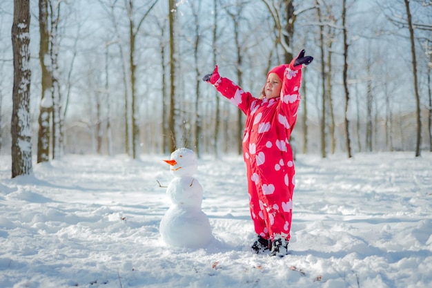 Kleines Mädchen, das Schneemann im verschneiten Park baut Aktive Freizeit im Freien mit Familie mit Kindern im Winter Kid während eines Spaziergangs in einem verschneiten Winterpark