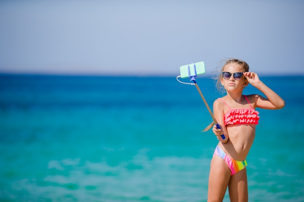 Kleines Mädchen, das selfie durch ihren Smartphone auf dem Strand nimmt.