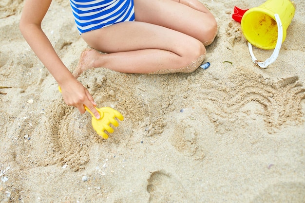 Kleines Mädchen, das sich am Strand amüsiert und mit Sand spielt, spielt Sommerurlaub mit der Familie Hintergrund mit leerem Platz für Text