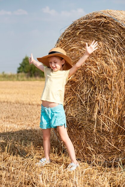 Kleines Mädchen, das sich an einem Sommertag auf einem Weizenfeld amüsiert. Kind, das während der Erntezeit am Heuballenfeld spielt.