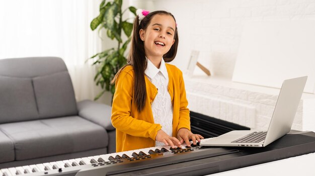 Kleines Mädchen, das sich Online-Lektionen anschaut, wie man einen Synthesizer lernt.
