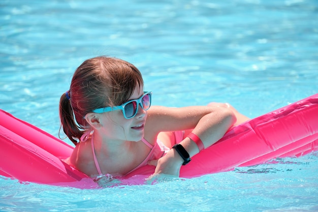 Kleines Mädchen, das sich während der tropischen Ferien auf der Sommersonne beim Schwimmen auf einer aufblasbaren Luftmatratze im Schwimmbad entspannt Sommerzeit-Aktivitäten-Konzept