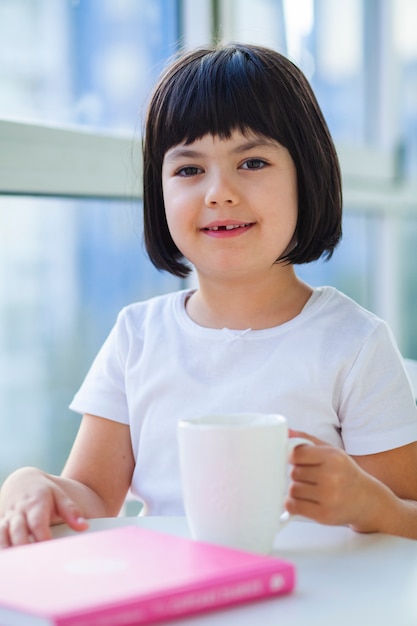 Kleines Mädchen, das Tee der Milch zu Hause trinkt