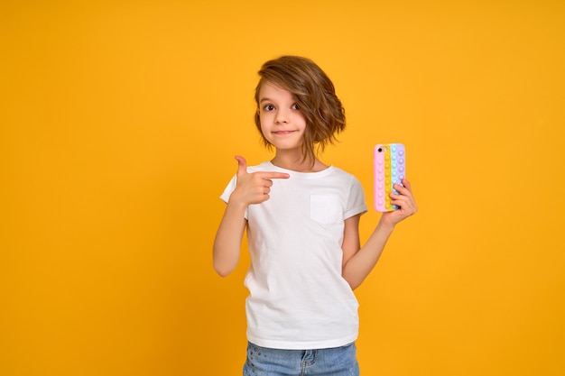 Kleines Mädchen, das Telefon hält und darauf zeigt, isoliert über orangefarbenem Hintergrund