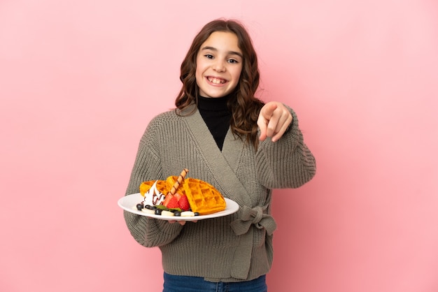 Kleines Mädchen, das Waffeln isoliert hält, überrascht und nach vorne zeigend