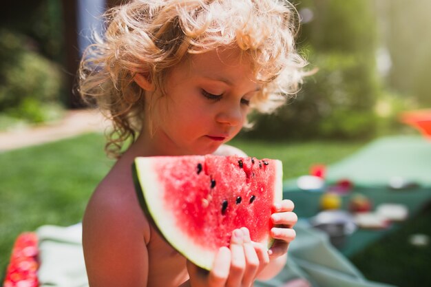 Kleines Mädchen, das Wassermelone auf dem Gras im Sommer isst