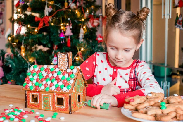 Kleines Mädchen, das Weihnachtslebkuchenhaus am Kamin in verziertem Wohnzimmer macht.