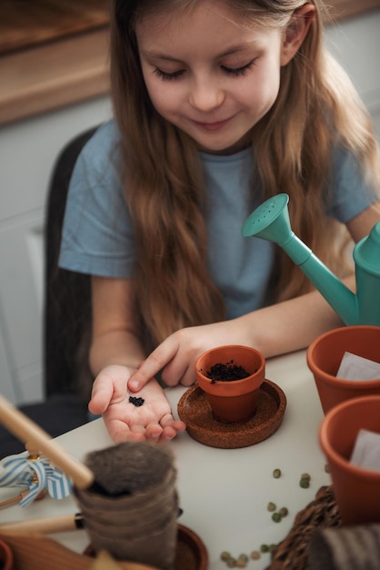 Kleines Mädchen, das zu Hause am Tisch sitzt und Samen in Blumentöpfe sät