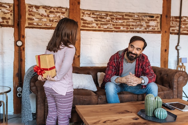 Kleines Mädchen, das zu Hause ein Überraschungsgeschenk O ihr Vater auf dem Sofa am Vatertag gibt