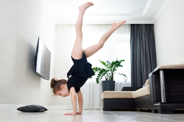 Kleines Mädchen, das zu Hause Gymnastik macht, die auf ihren Händen kopfüber steht